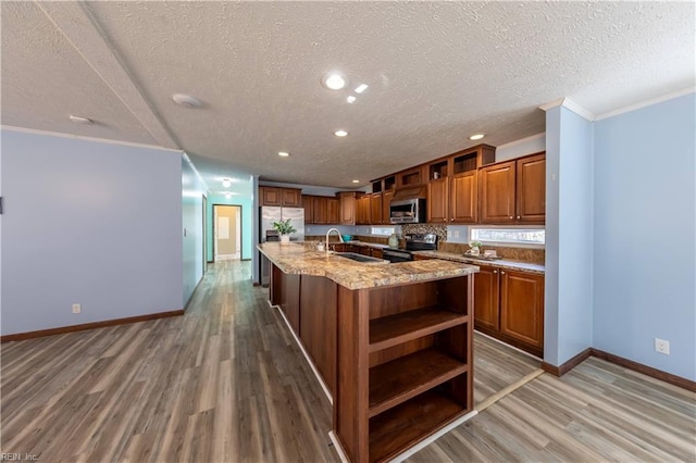 kitchen featuring brown cabinets, open shelves, appliances with stainless steel finishes, a kitchen island with sink, and a sink