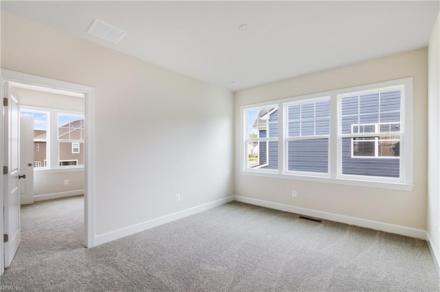 empty room featuring a wealth of natural light, visible vents, light carpet, and baseboards