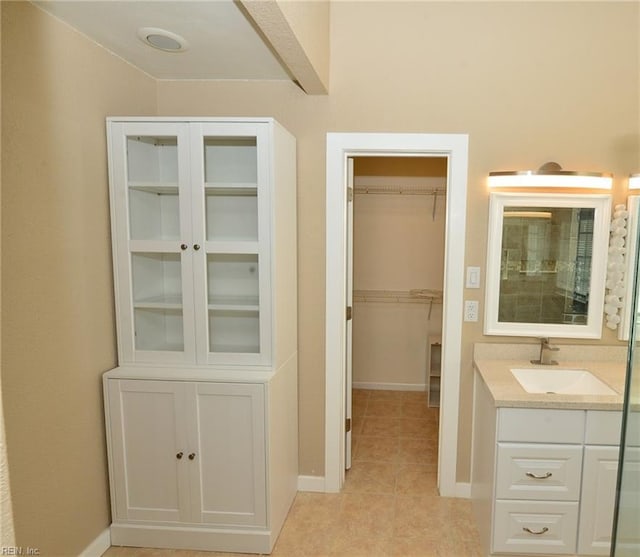 bathroom with tile patterned flooring, baseboards, a walk in closet, and vanity