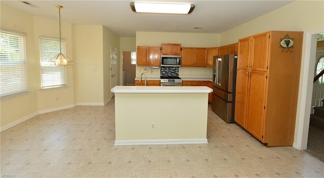 kitchen with pendant lighting, light floors, light countertops, appliances with stainless steel finishes, and an island with sink