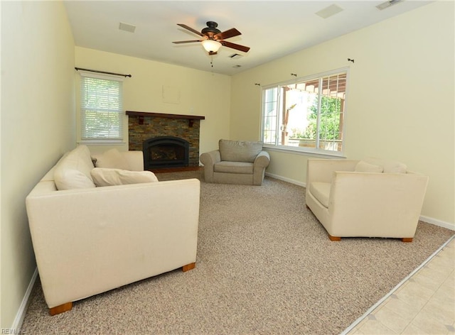 tiled living area with a ceiling fan, plenty of natural light, a stone fireplace, and baseboards