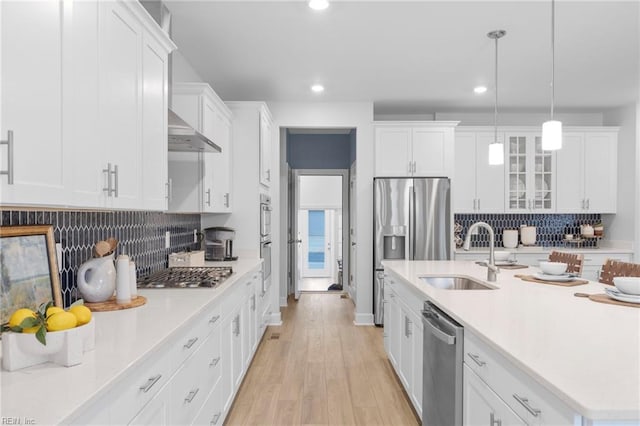 kitchen with decorative light fixtures, a sink, light countertops, appliances with stainless steel finishes, and glass insert cabinets