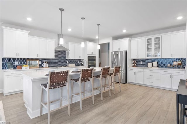 kitchen featuring wall chimney exhaust hood, appliances with stainless steel finishes, decorative light fixtures, light countertops, and white cabinetry