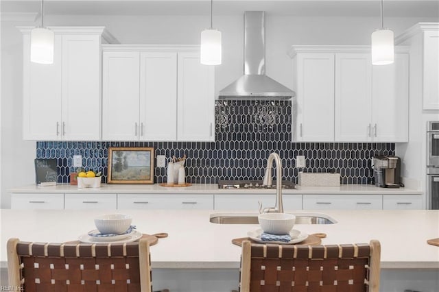 kitchen with decorative backsplash, wall chimney exhaust hood, hanging light fixtures, light countertops, and white cabinetry