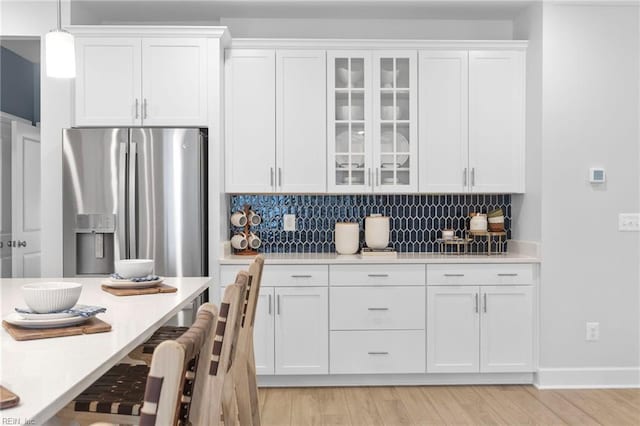 kitchen featuring glass insert cabinets, white cabinets, light countertops, stainless steel fridge with ice dispenser, and decorative light fixtures