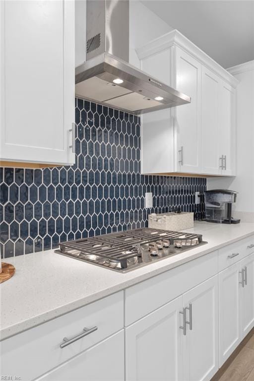 kitchen with light stone counters, range hood, stainless steel gas cooktop, decorative backsplash, and white cabinetry