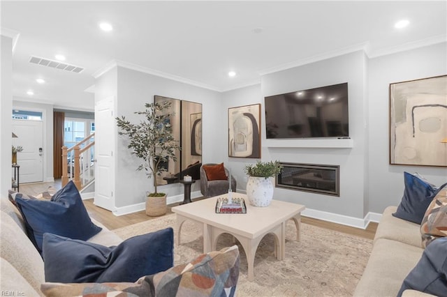 living area with a glass covered fireplace, visible vents, light wood-style flooring, and stairs