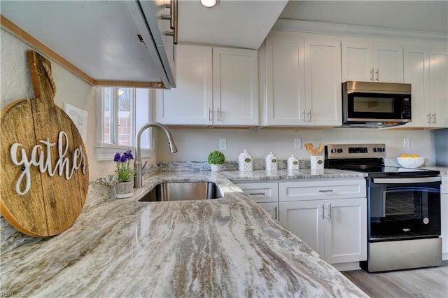 kitchen featuring light stone counters, stainless steel appliances, light wood-style flooring, white cabinets, and a sink