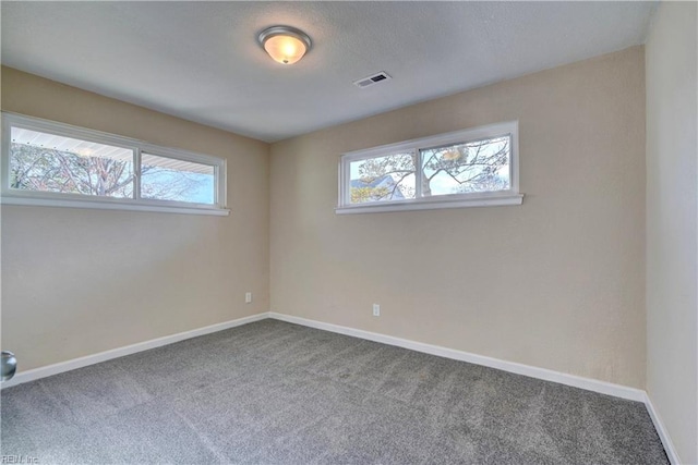 carpeted spare room with a healthy amount of sunlight, visible vents, and baseboards