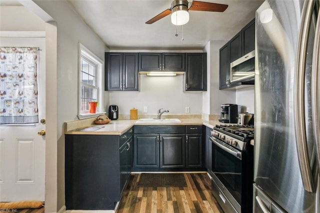 kitchen with stainless steel appliances, light countertops, dark wood-type flooring, a ceiling fan, and a sink