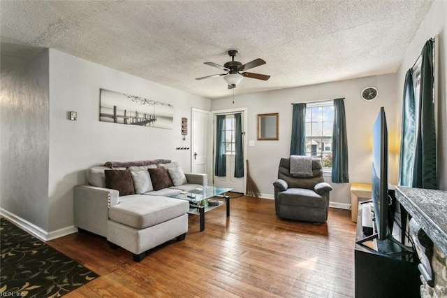 living area featuring a ceiling fan, dark wood finished floors, a textured ceiling, and baseboards