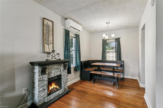 living area with a wall unit AC, an inviting chandelier, a stone fireplace, wood finished floors, and baseboards