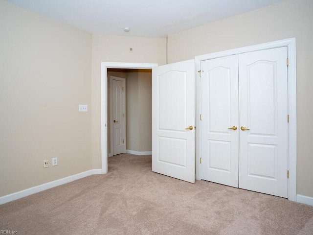 unfurnished bedroom with a closet, light colored carpet, and baseboards