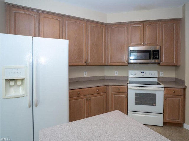 kitchen featuring white appliances, light tile patterned floors, light countertops, and brown cabinetry