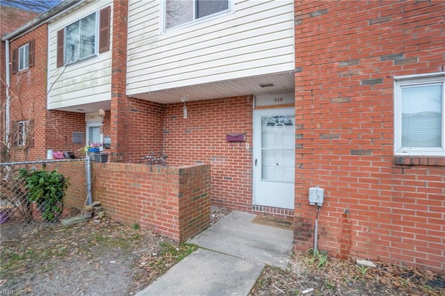 view of exterior entry featuring brick siding and fence