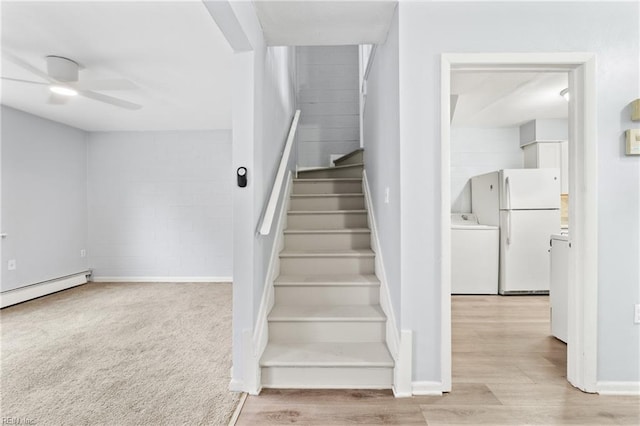 stairway featuring washer / clothes dryer, a ceiling fan, a baseboard heating unit, wood finished floors, and baseboards