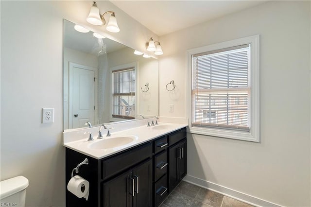 bathroom featuring toilet, a sink, baseboards, and double vanity