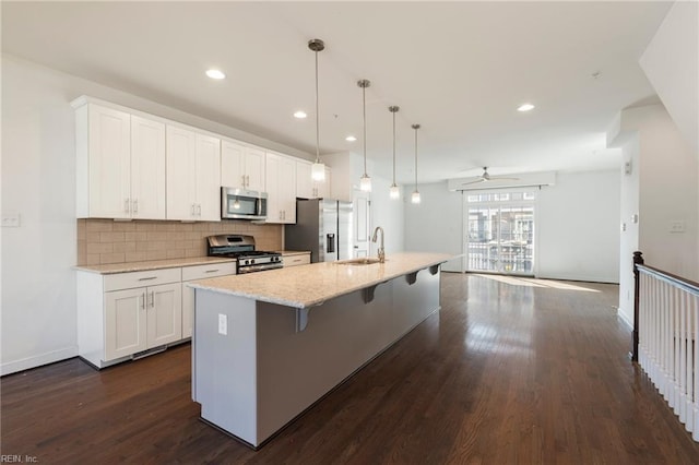 kitchen featuring an island with sink, appliances with stainless steel finishes, a kitchen breakfast bar, decorative light fixtures, and white cabinetry