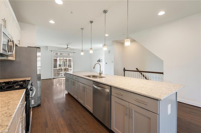 kitchen with a kitchen island with sink, dark wood-style flooring, a sink, appliances with stainless steel finishes, and pendant lighting