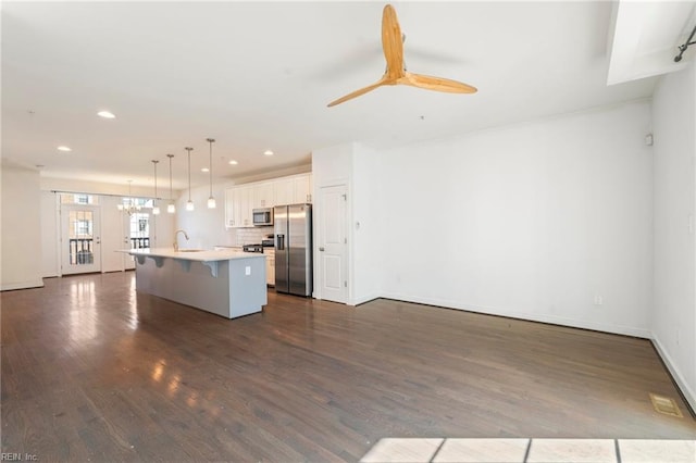 kitchen featuring a breakfast bar area, open floor plan, hanging light fixtures, appliances with stainless steel finishes, and a center island with sink