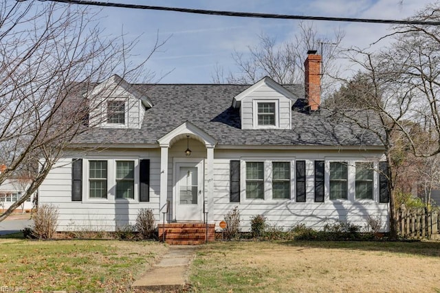 new england style home with entry steps, roof with shingles, a chimney, and a front yard