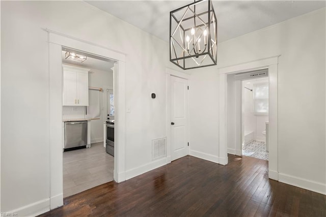 unfurnished dining area with visible vents, dark wood finished floors, a notable chandelier, and baseboards