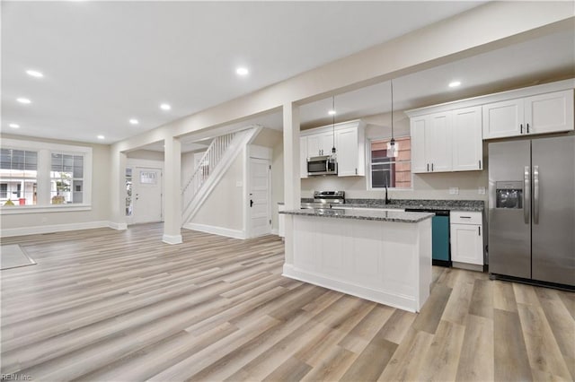 kitchen featuring a center island, decorative light fixtures, stainless steel appliances, white cabinetry, and dark stone counters