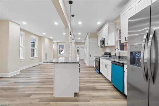 kitchen with white cabinetry, appliances with stainless steel finishes, light stone counters, and a center island