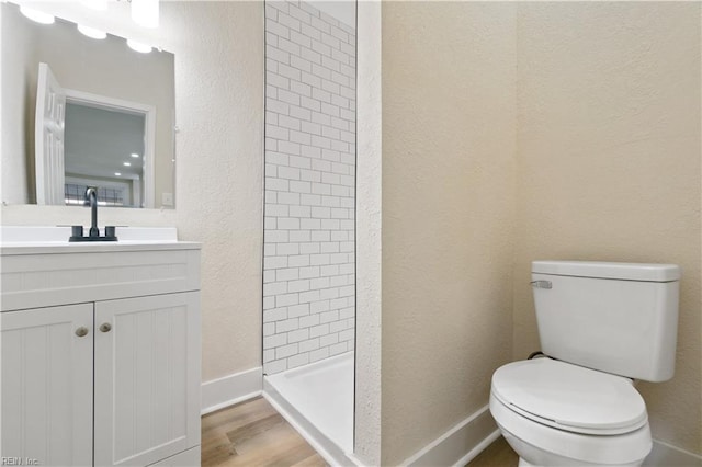 full bath featuring toilet, vanity, wood finished floors, tiled shower, and baseboards