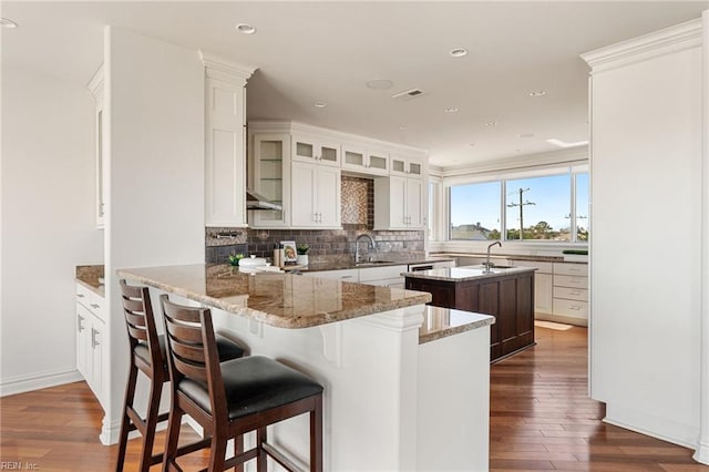 kitchen featuring glass insert cabinets, white cabinets, a sink, and a peninsula