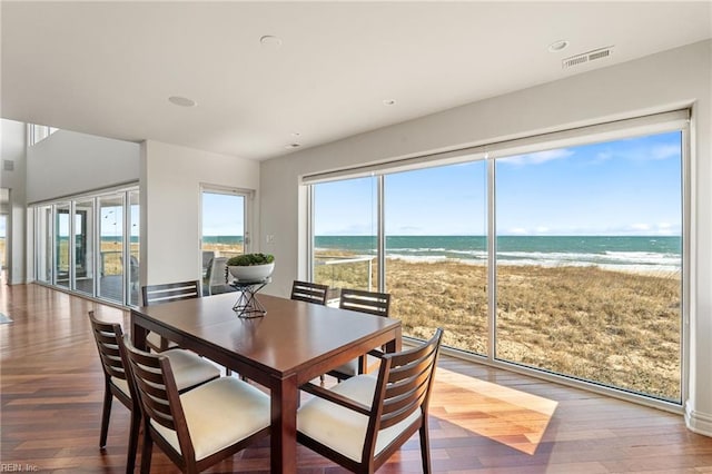 dining space with visible vents, a water view, a beach view, and wood finished floors