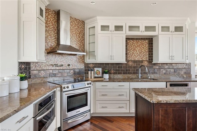 kitchen with wall chimney exhaust hood, appliances with stainless steel finishes, glass insert cabinets, and a sink