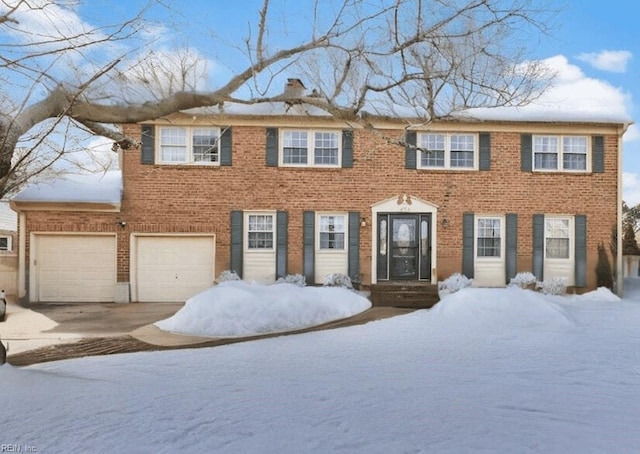 colonial inspired home with brick siding, driveway, a chimney, and an attached garage