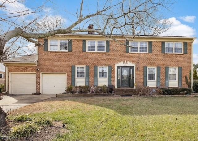 colonial-style house with brick siding, a chimney, concrete driveway, and a front yard