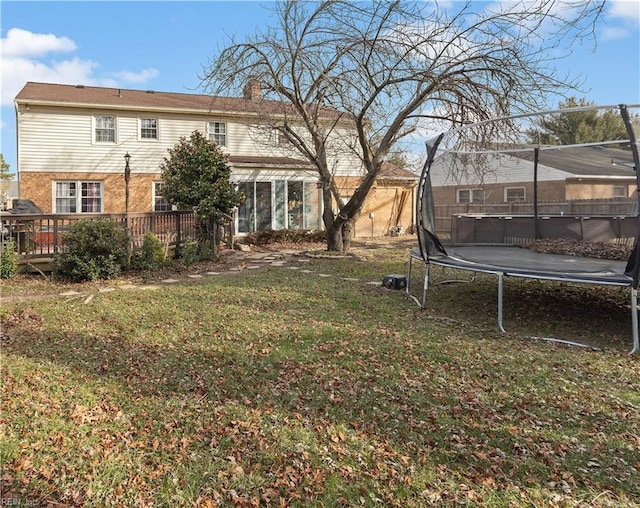 view of yard featuring a trampoline, a wooden deck, and fence