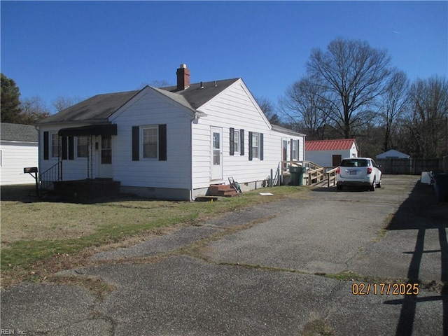 view of property exterior with an outbuilding, a yard, a chimney, entry steps, and driveway