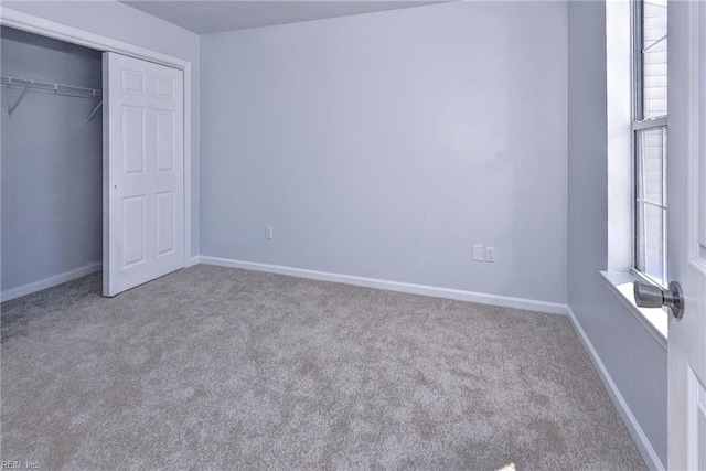 unfurnished bedroom featuring light carpet, multiple windows, a closet, and baseboards