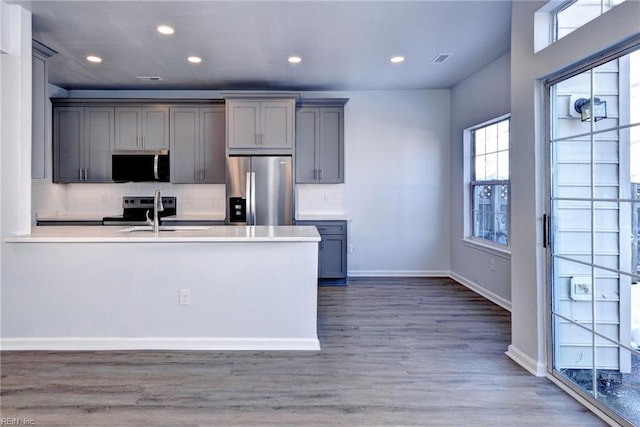 kitchen with dark wood-style floors, stainless steel appliances, gray cabinets, light countertops, and decorative backsplash