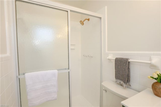 full bathroom with a stall shower, wainscoting, tile walls, and toilet