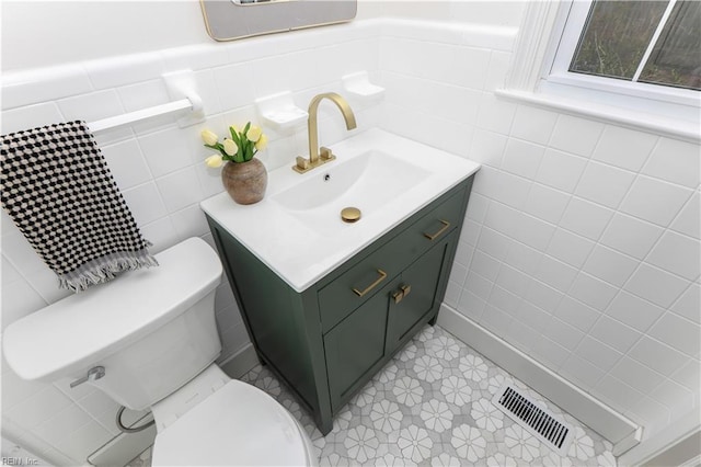 bathroom featuring toilet, vanity, visible vents, and tile walls