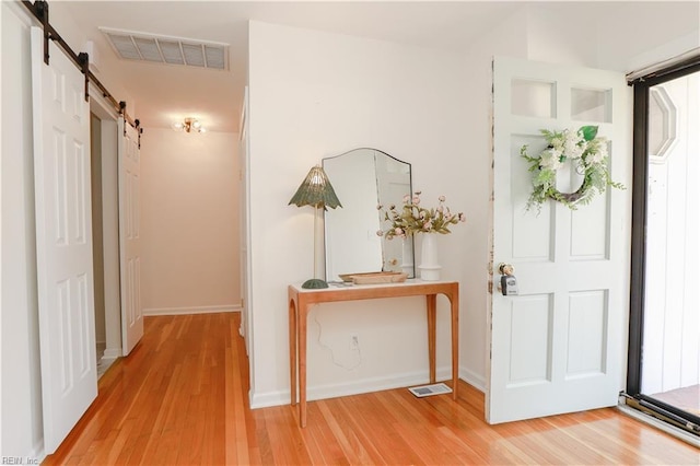 foyer entrance featuring baseboards, a barn door, visible vents, and wood finished floors