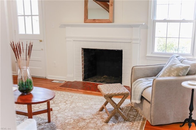 living area with a brick fireplace, wood finished floors, visible vents, and baseboards