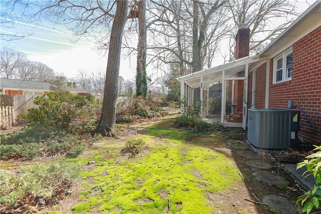 view of yard with fence, a sunroom, and central air condition unit