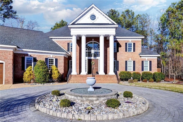 greek revival inspired property featuring a shingled roof, brick siding, and curved driveway