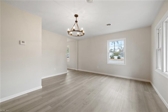 spare room with an inviting chandelier, visible vents, baseboards, and wood finished floors