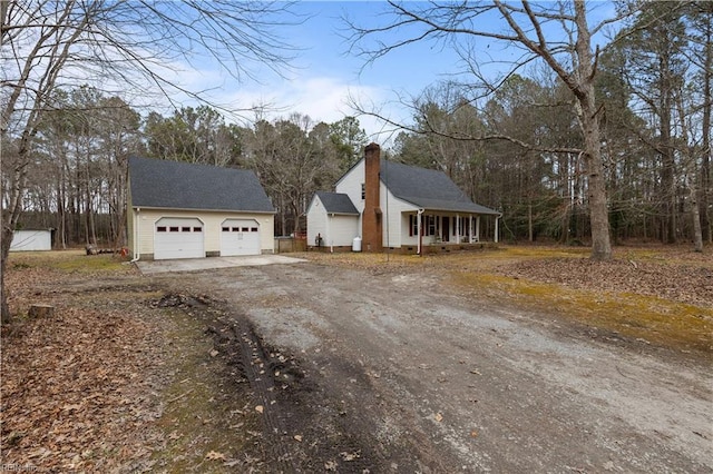 view of front of house with driveway, a garage, a chimney, covered porch, and an outdoor structure