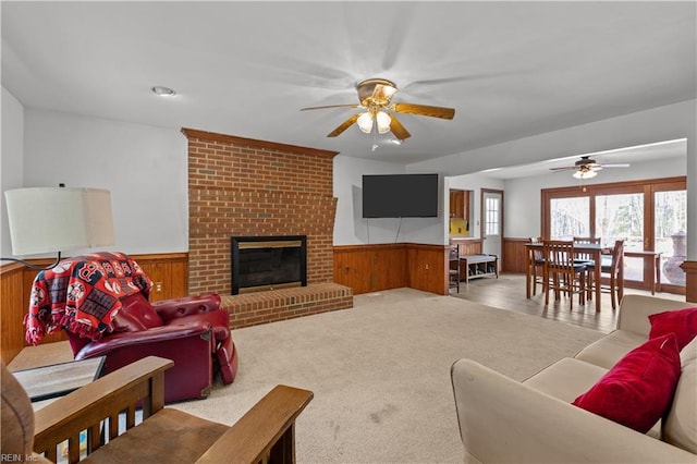 carpeted living area featuring a brick fireplace, wainscoting, and ceiling fan