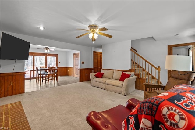 living area with ceiling fan, a wainscoted wall, carpet floors, wood walls, and stairway