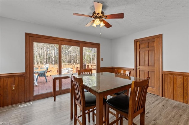 dining space featuring light wood-type flooring, a wainscoted wall, and visible vents