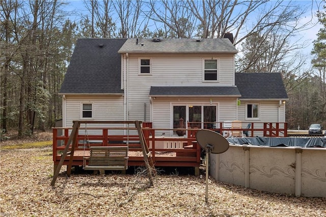 back of house with a covered pool, a deck, and a shingled roof